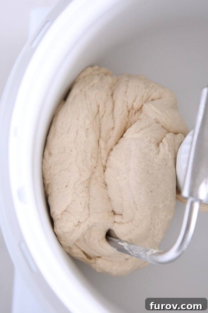 Pillowy Soft Homemade Pretzels 4 A soft, perfectly formed ball of pretzel dough sitting in a white Bosch universal mixer bowl with the dough hook attached.