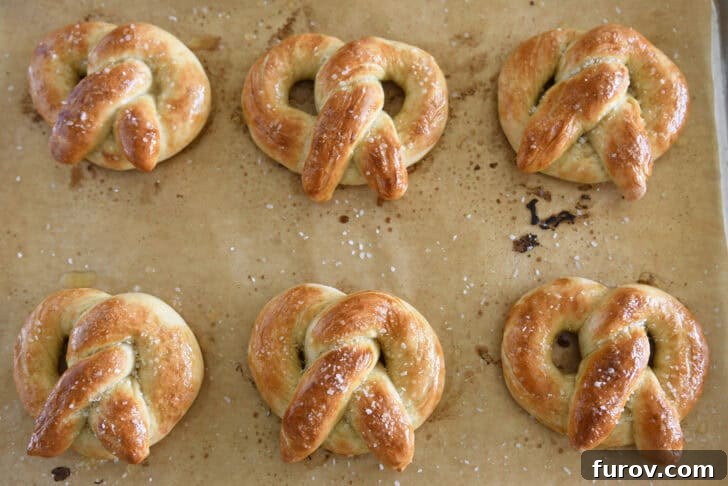 Pillowy Soft Homemade Pretzels 6 Six golden-brown, home-baked soft pretzels arranged on a parchment-lined baking sheet and lightly sprinkled with salt.