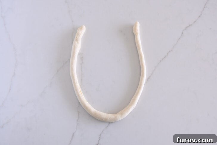 Pillowy Soft Homemade Pretzels 8 A long, thin rope of pretzel dough skillfully formed into a horseshoe shape, preparing for the twist.