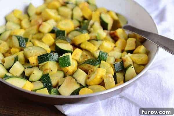 A skillet full of sautéed zucchini and yellow squash, with a full spoonful of the saute on top of the mixture.