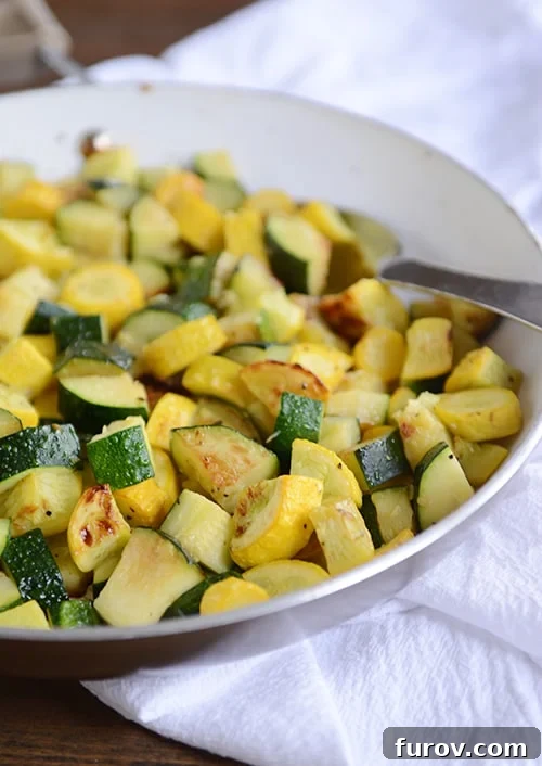 A skillet full of sautéed zucchini and yellow squash, with a full spoonful of the saute on top of the mixture.