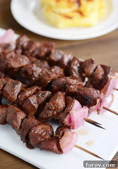 A white tray of succulent beef and onion kebabs, fresh off the grill.