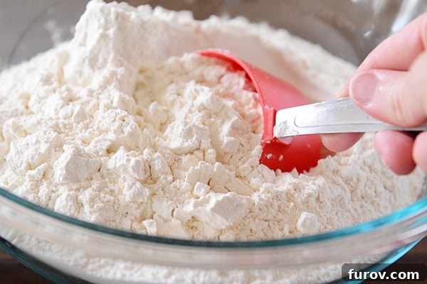 A red measuring cup scooping out flour from a glass bowl.