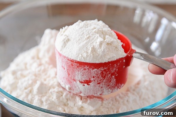 A heaping cupful of flour over a bowl of flour. 