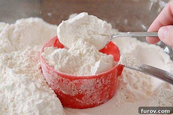 A spoon scooping flour into a red measuring cup. 