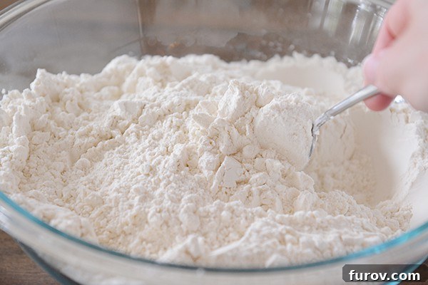 A spoon stirring a clear bowl of white flour. 