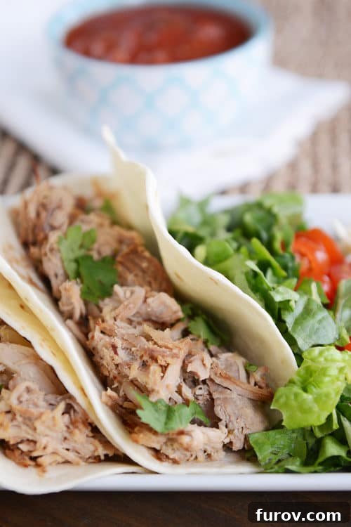 Melt-in-Your-Mouth Slow Cooker Carnitas 2 A shredded pork taco in a flour tortilla next to fresh lettuce and tomatoes, ready to be assembled.