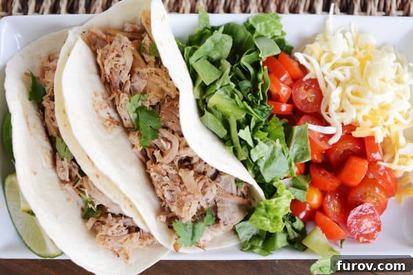 Melt-in-Your-Mouth Slow Cooker Carnitas 3 A white serving tray filled with shredded pork tacos, alongside a fresh green salad, cherry tomatoes, and shredded cheese.