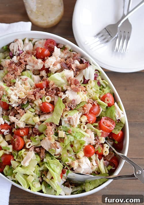 Portillos Iconic Chopped Salad with Signature Sweet Italian Dressing 2 A large oval bowl full of Portillo's chopped salad with bacon, tomatoes, and chicken on top.