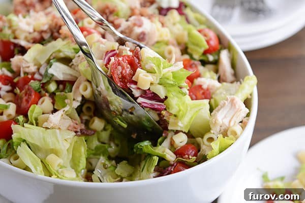 Portillos Iconic Chopped Salad with Signature Sweet Italian Dressing 4 A white bowl of chicken, pasta, and tomato chopped salad.