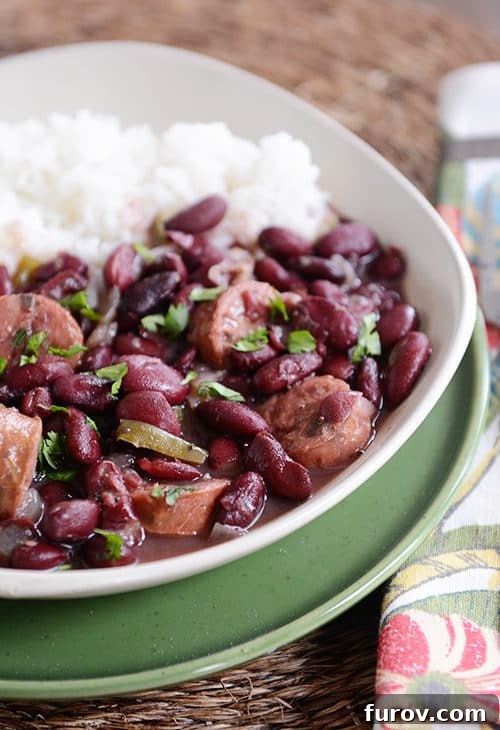 Hearty Slow Cooker Red Beans and Rice with Chicken Sausage 2 A white bowl of cooked red beans and chicken sausage next to white rice.