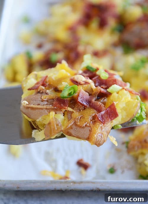 Ultimate Cheesy Bacon Garlic Smashed Reds 3 A metal spatula carefully lifting a single cheesy, bacon, and garlic butter smashed red potato from a baking sheet, showcasing its crispy bottom and melted toppings.