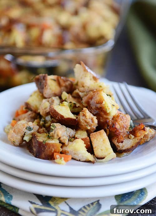 Savory Pretzel Sausage Stuffing 3 A white plate showcasing a generous serving of pretzel roll and sausage stuffing, with a fork resting beside it.