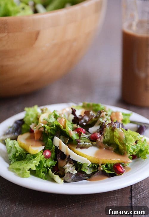 A green Autumn salad topped with dressing and fruit on a white plate, showcasing vibrant fall colors.