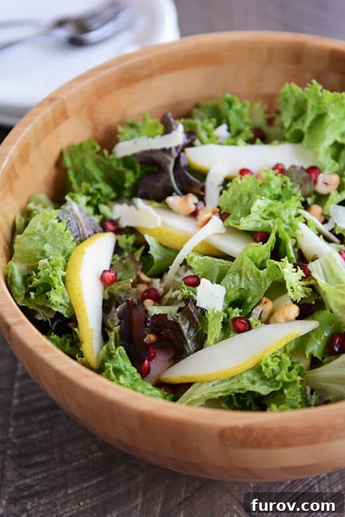 A wooden salad bowl full of a green salad topped with sliced pears, nuts, and shredded parmesan, ready to be served.