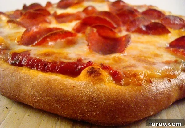 Close-up side view of a perfectly cooked pepperoni pizza with a golden, airy crust.