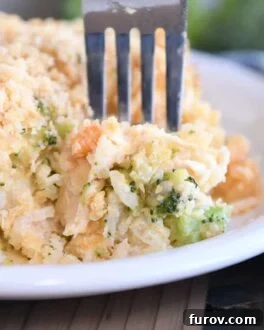 Fork scooping a bite of cheesy casserole with rice, broccoli, and carrots on a white plate.