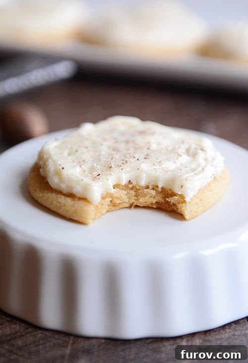 A perfectly frosted soft eggnog sugar cookie with a bite taken out, resting on an upside-down ramekin.