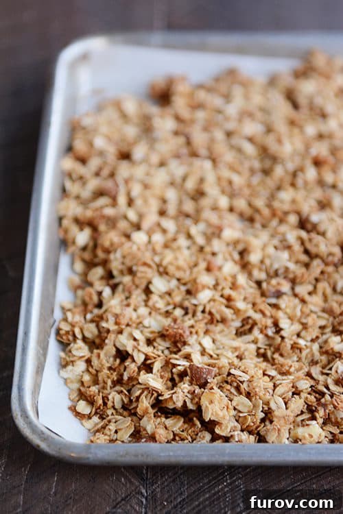 A cookie sheet of baked almond granola, golden brown and perfectly clustered.