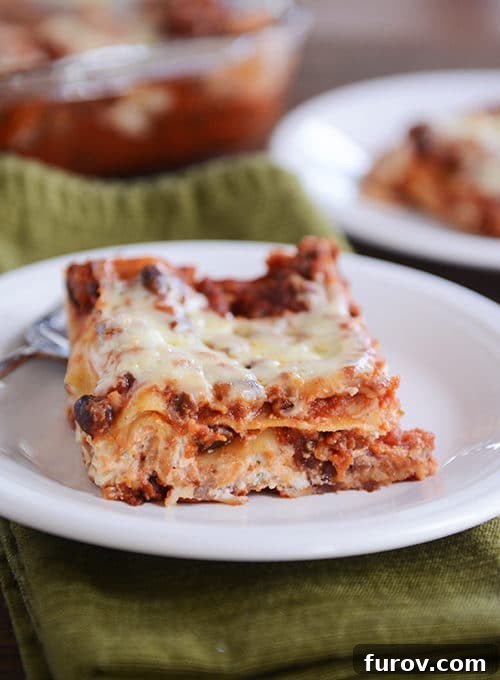 A perfectly portioned square of cheesy black bean lasagna on a clean white plate, showcasing the rich layers of pasta, savory black bean sauce, and melted cheese.