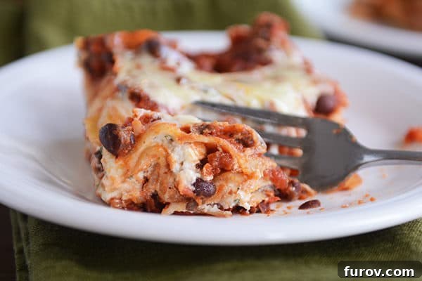 A mouthwatering square of cheesy black bean lasagna served on a white plate, with a fork gently taking a bite, revealing the gooey, melted cheese and rich bean filling.