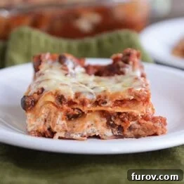 Close-up image of a single slice of cheesy black bean lasagna on a plate, highlighting the delicious texture of the melted cheese and a glimpse of the rich bean filling.