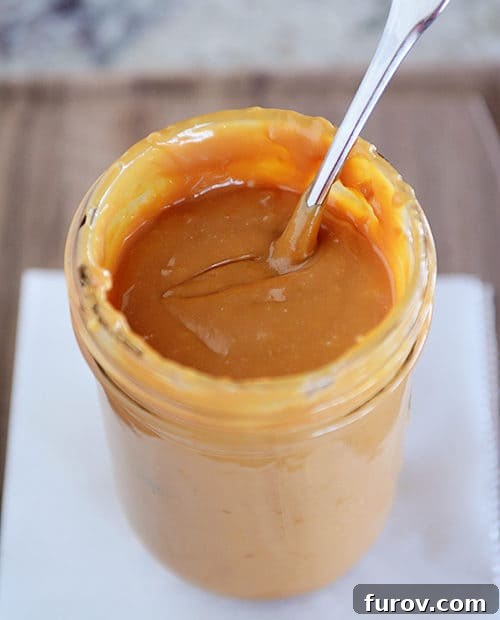 Dulce de Leche in the Instant Pot and Stovetop Pressure Cooker 10 A mason jar filled with perfectly golden-brown dulce de leche, with a spoon inserted, tempting a taste.