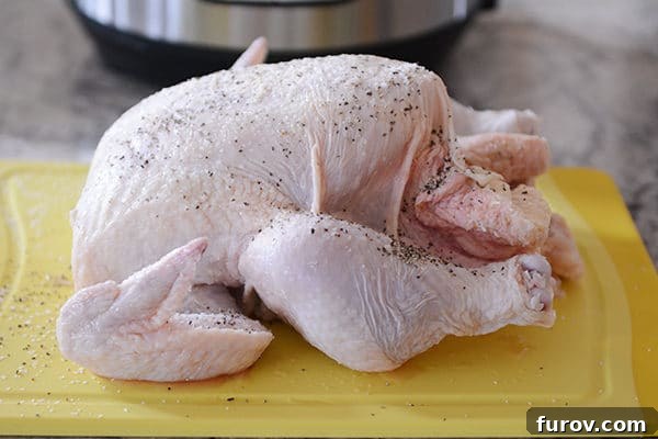 A raw whole chicken, sprinkled with pepper, on a yellow cutting board. 