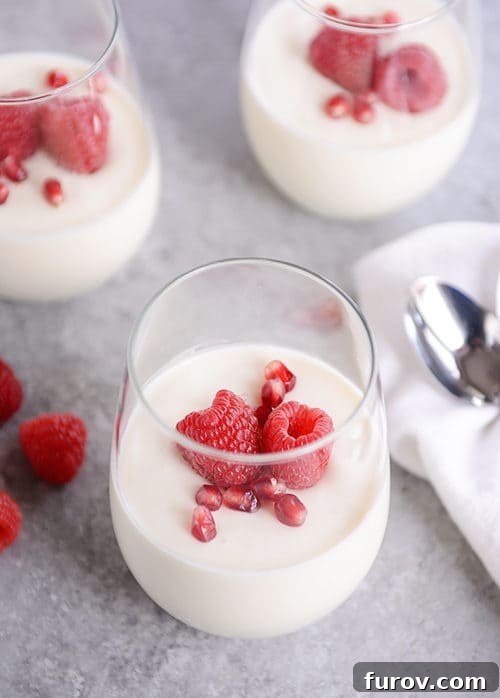 Glasses of cream topped with pomegranate seeds and raspberries.