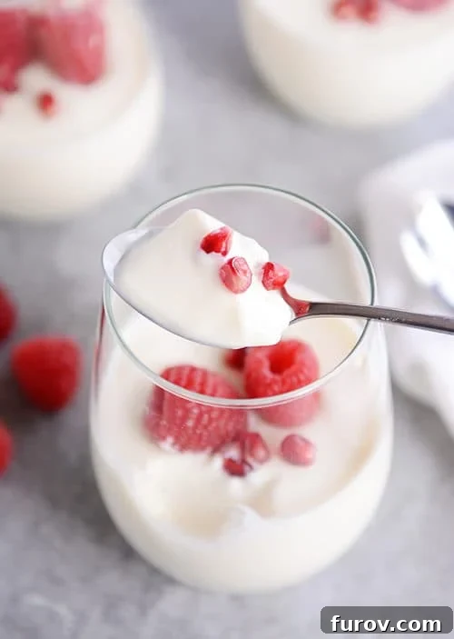 A spoon taking a bite of cream and berries out of a glass cup. 