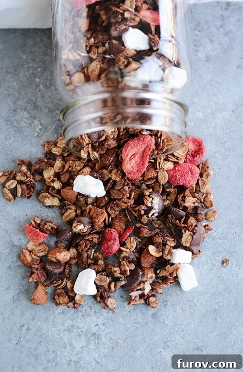 Dark chocolate and strawberry granola spilling out of a glass mason jar.