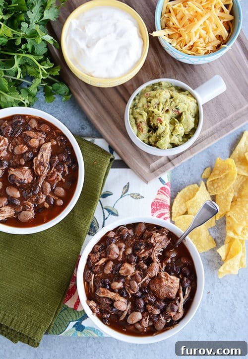An inviting overhead view of several bowls of chicken black bean chili, artfully arranged with separate bowls of fresh, colorful toppings including shredded cheese, creamy sour cream, and vibrant green guacamole.
