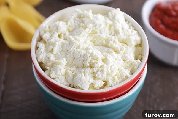 Close-up shot of a red bowl overflowing with fluffy, white homemade ricotta cheese.