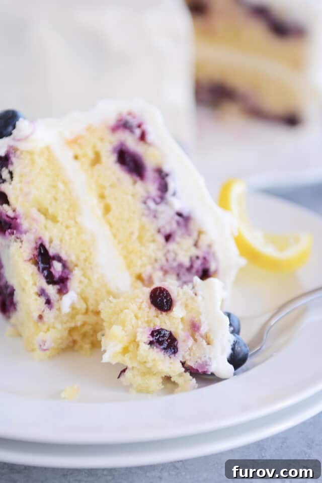 A delectable slice of lemon blueberry cake on a white plate, with a bite taken, showcasing its moist texture and juicy blueberries.