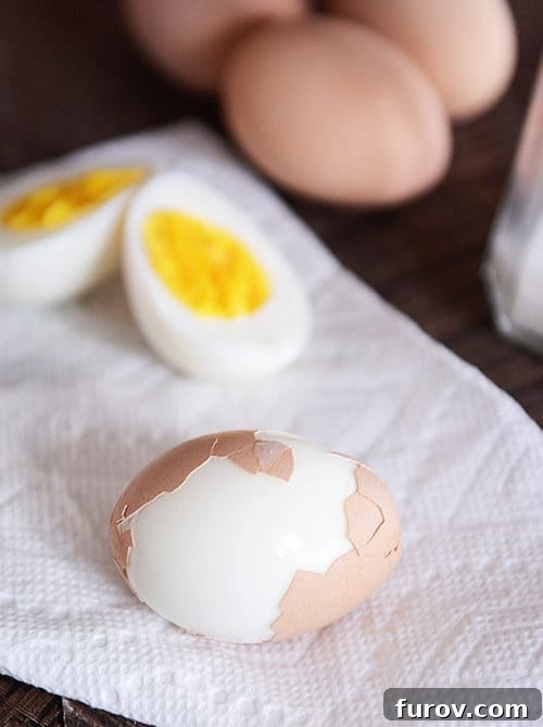 A perfectly hard-boiled egg, sliced in half, revealing a vibrant yellow yolk. Next to it, another egg is partially peeled, showcasing its smooth, unblemished white.