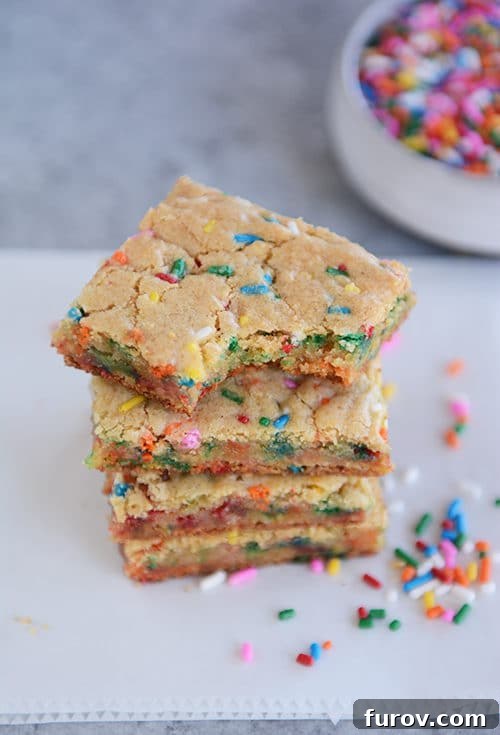 Funfetti blondie bars stacked on top of each other with the top bar with a bite taken out.