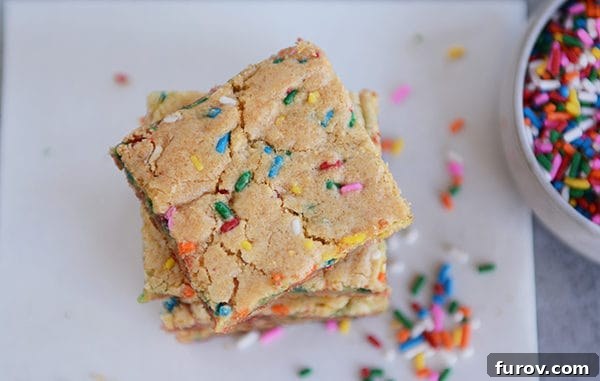 Sprinkle-filled blondie bars stacked on each other on a piece of parchment.