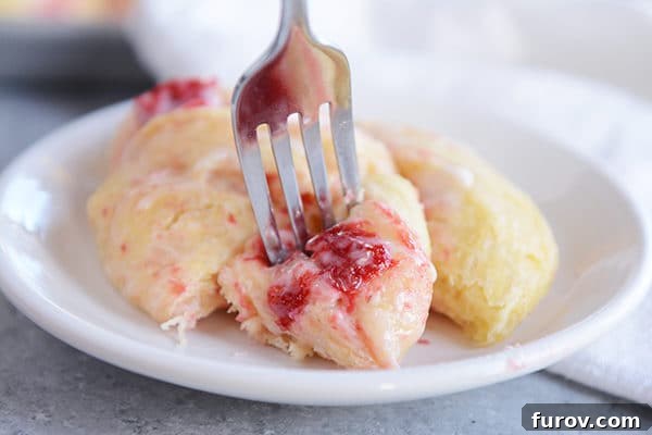 A strawberry cream cheese roll on a plate with one bite cut out on a fork, ready to eat.