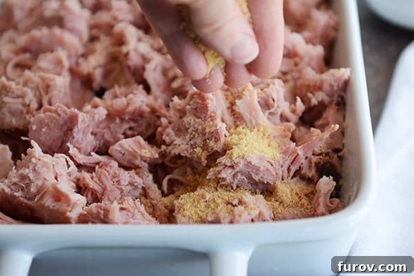 Sweet Glazed Ham in the Instant Pot 3 A white dish full of shredded, baked ham with seasoning being sprinkled on the top.