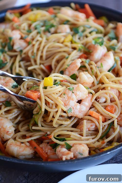 Fast Asian Garlic Noodles with Your Choice of Shrimp or Chicken 2 A skillet brimming with perfectly cooked spaghetti noodles, succulent shrimp, and a colorful array of chopped vegetables, all coated in a rich and glossy Asian garlic sauce, ready to be served.