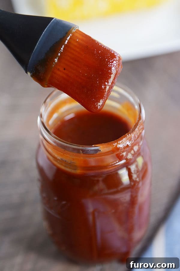 The Secret to Irresistible Homemade Barbecue Sauce 2 A mason jar full of BBQ sauce, with a drip coming down the side and a pastry brush with sauce over the top.