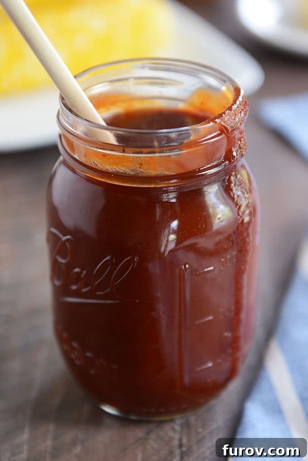 The Secret to Irresistible Homemade Barbecue Sauce 3 A mason jar full of BBQ sauce, with a drip coming down the side and a wooden spoon in the jar.