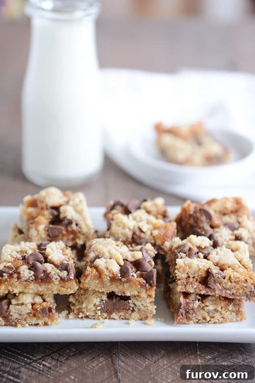 Gooey Chocolate Chip Caramel Cookie Bars 2 Caramel chocolate chip cookie bars on a white platter in front of a glass jar of milk.