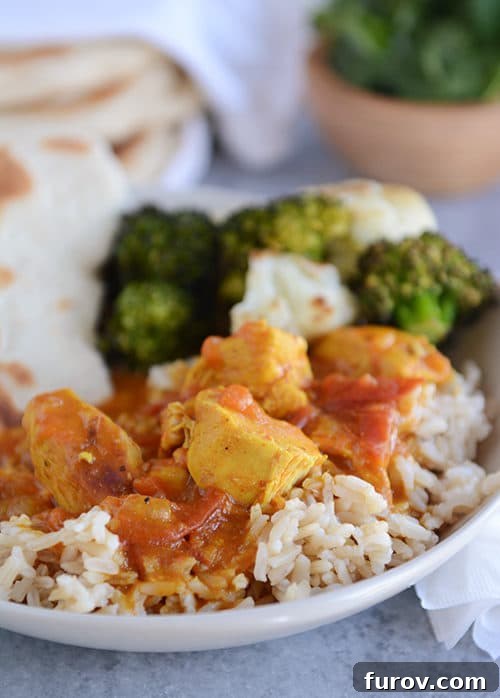 A beautiful white bowl filled with fluffy rice, topped generously with creamy chicken coconut curry, fresh green herbs, and vibrant red chili flakes for garnish.