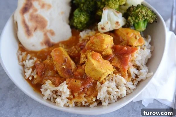 An overhead shot of a generous serving of chicken coconut curry with fluffy white rice, garnished with fresh cilantro and a side of warm naan bread on a rustic wooden surface.