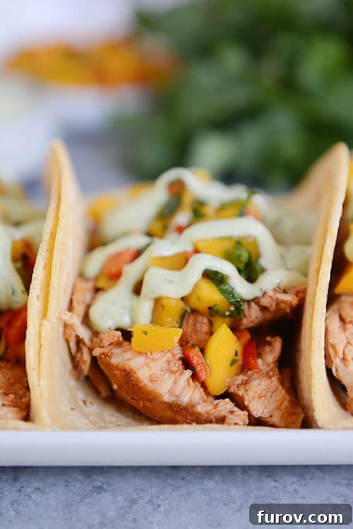 A vibrant pork taco in a soft corn tortilla, generously topped with fresh mango salsa and a creamy green dressing, resting on a white plate.