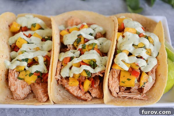 An overhead view of several pork and vegetable tacos, beautifully arranged on a white platter and artfully drizzled with a bright green avocado dressing.
