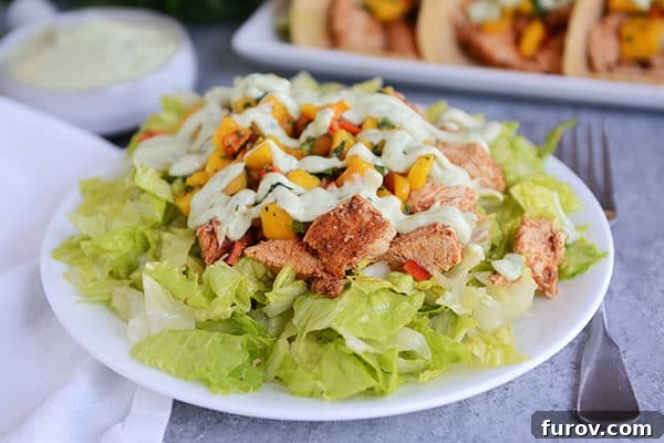 A refreshing green salad generously topped with succulent chicken and a medley of colorful vegetables, served on a crisp white plate.