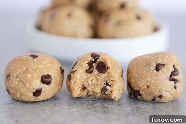 Three perfectly rolled cookie dough bites lined up, with the middle one showing a delectable bite taken out.