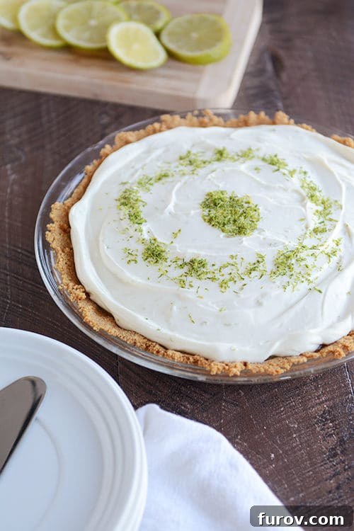 Zesty Key Lime White Chocolate Cheesecake Indulgence 3 A stunning Key Lime White Chocolate Cheesecake Pie, beautifully topped with a swirl of white chocolate and a generous sprinkle of fresh lime zest, ready to be served.